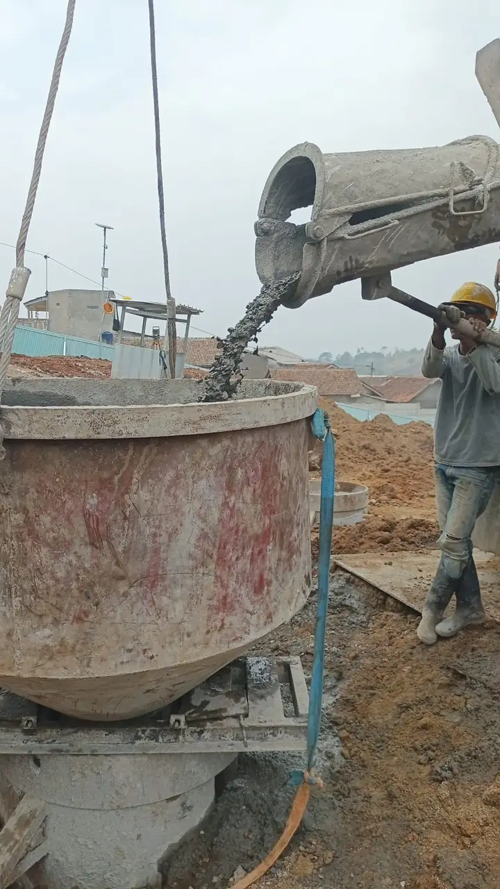 Beton ready-mix dituang dari truk ke hopper tremie di atas lubang bored pile