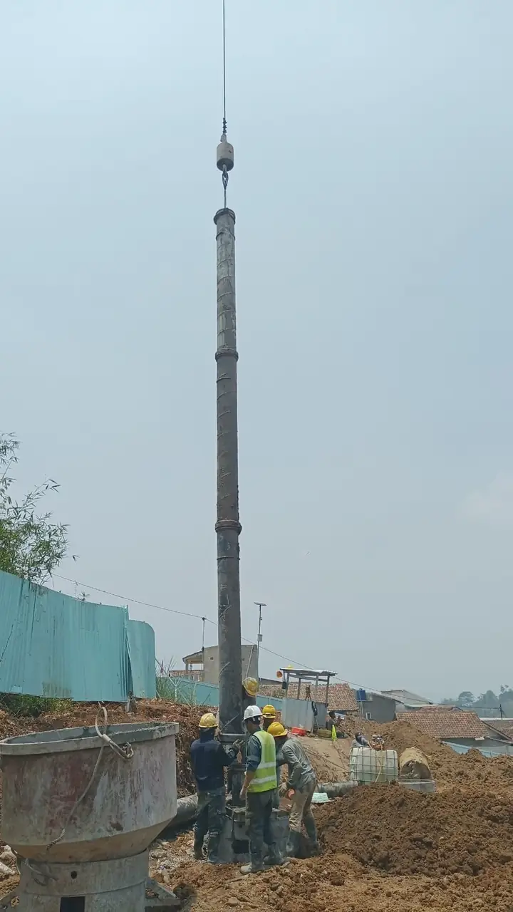 Rangkaian pipa tremie digantung crane di atas lubang bored pile, dipegang pekerja