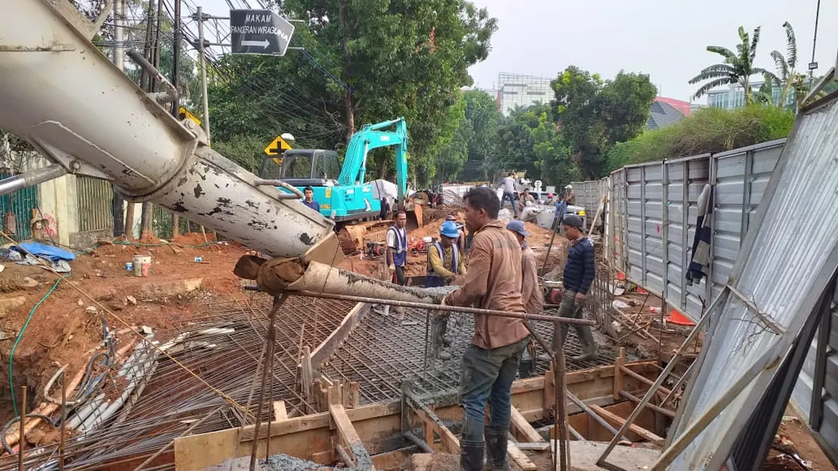 Pekerjaan pondasi di badan jalan dengan pagar pengaman, pompa beton, dan lalu lintas yang tetap berjalan di sisi lain