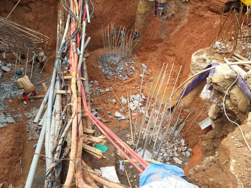 Berkas kabel dan pipa eksisting menyilang di atas galian, digantung agar tetap aman selama pekerjaan