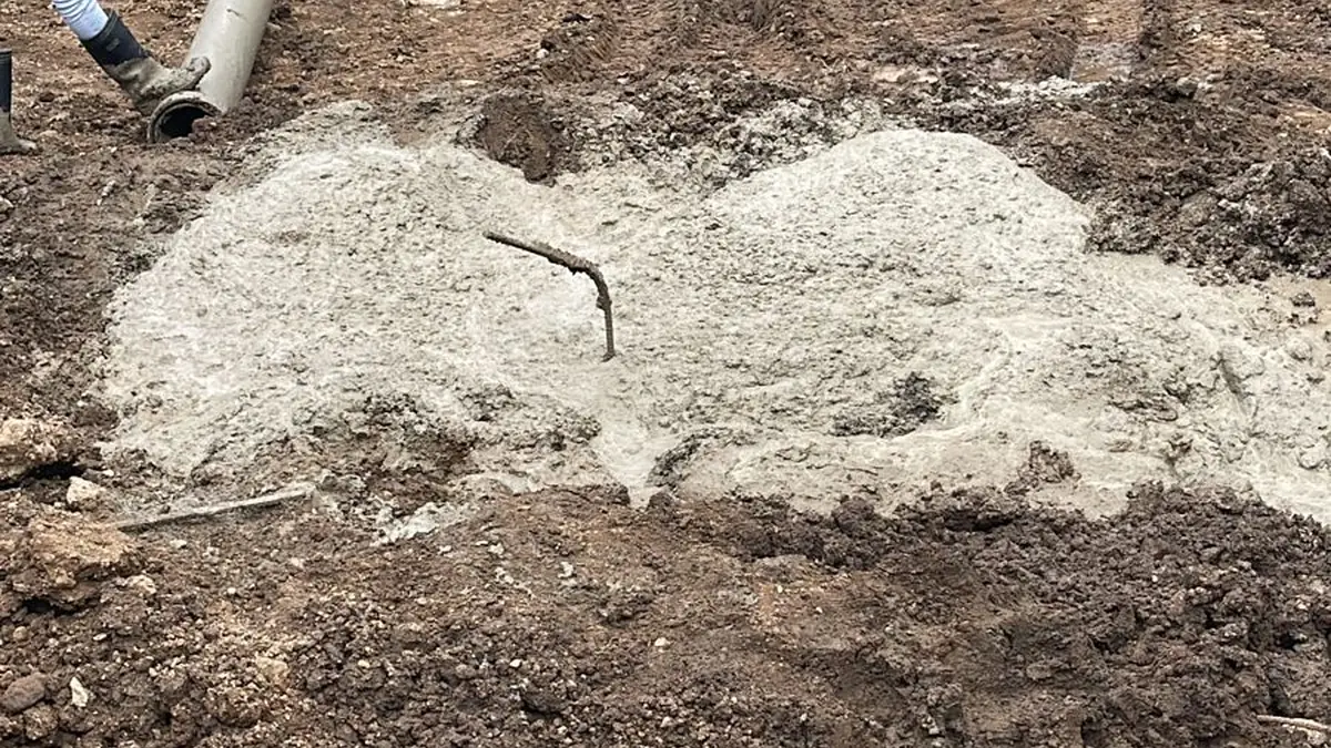 Kepala tiang bor yang baru selesai dicor di area kerja, dengan rig bor di latar belakang