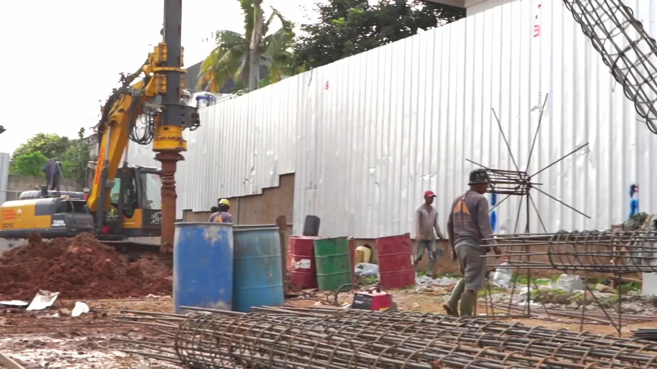 Rig bor bekerja di balik pagar seng dengan keranjang tulangan soldier pile tersusun di halaman