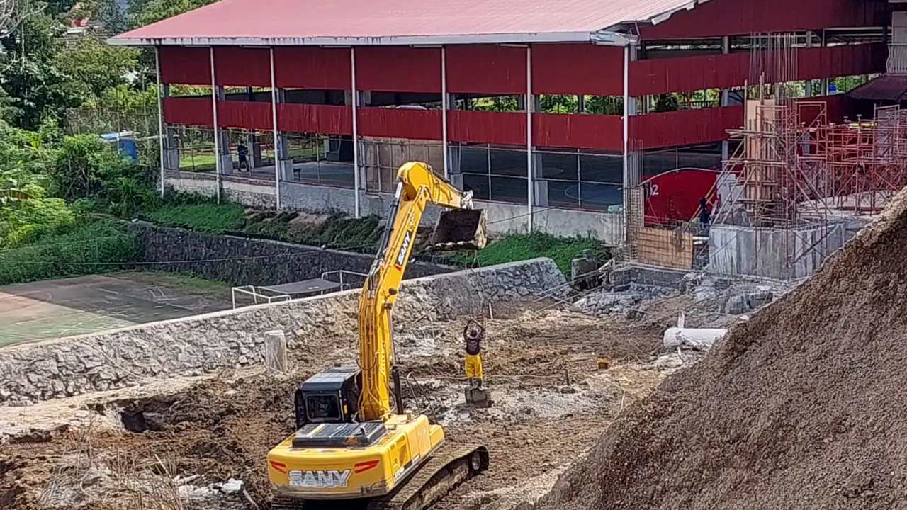 万雅老 Citra Kasih 学校新教学楼基础施工区内作业的挖掘机，背景为学校建筑